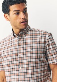 Chemise à manches courtes à carreaux dans des tons rose clair, marine et blanc, avec un col boutonné et un petit logo sur la poitrine.