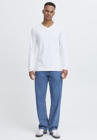 White long-sleeve V-neck shirt paired with light blue denim jeans. Casual fit with a smooth texture. Sneakers with black and white accents.
