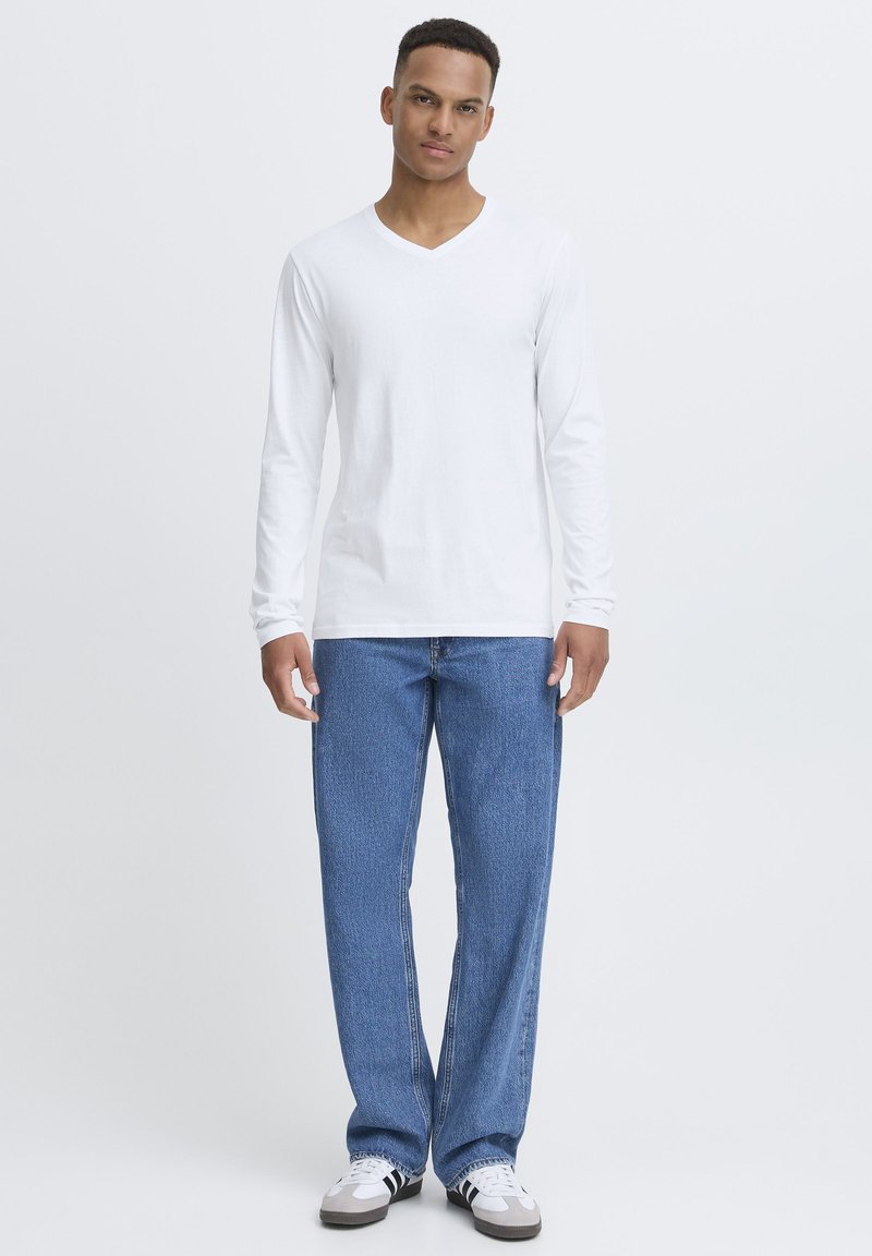 White long-sleeve V-neck shirt paired with light blue denim jeans. Casual fit with a smooth texture. Sneakers with black and white accents.