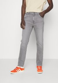 Vaqueros gris con corte de pierna recta, cinco bolsillos y textura clásica de mezclilla. Combinados con zapatillas de deporte de color naranja brillante.