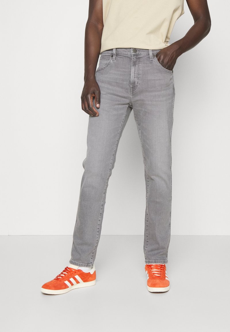 Vaqueros gris con corte de pierna recta, cinco bolsillos y textura clásica de mezclilla. Combinados con zapatillas de deporte de color naranja brillante.