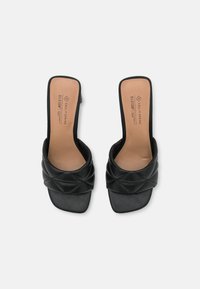 Zwarte hoge hakken sandalen met een gewatteerde bovenkant, open teenontwerp en vierkante hak. Glad oppervlak en tan kleurige binnenzool met merklogo.