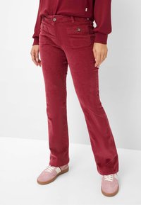 Rode corduroy broek met een rechte pasvorm, voorzien van twee voorkraagzakken, contrastknopen en een zachte textuur. Combinatie met roze sneakers.