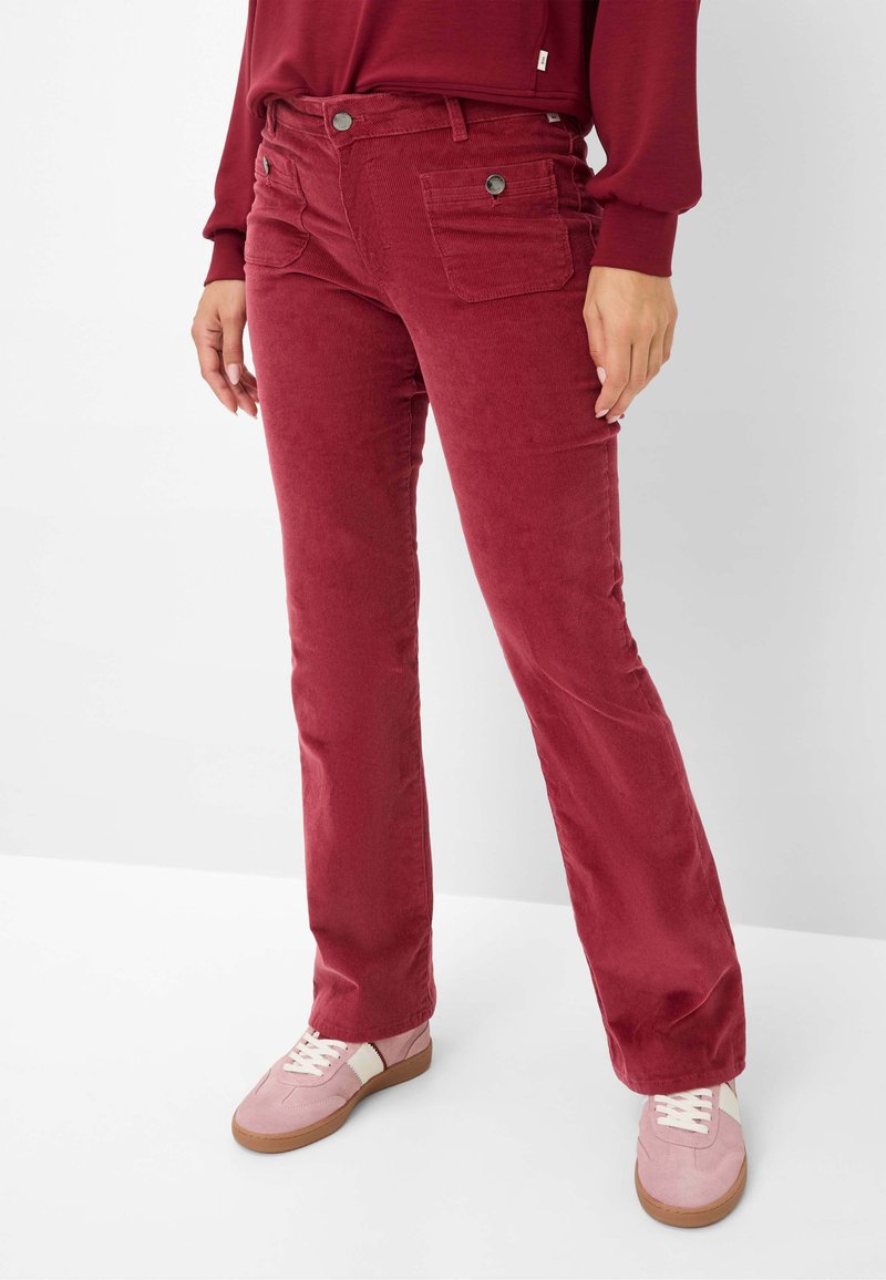 Rode corduroy broek met een rechte pasvorm, voorzien van twee voorkraagzakken, contrastknopen en een zachte textuur. Combinatie met roze sneakers.