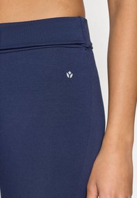 Legíny námorníckej modrej farby s hladkým povrchom, so sklopeným pásom a malým bielym logom na ľavej strane.