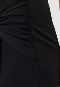 Vestito nero con tessuto arricciato e plissettato sul lato, caratterizzato da una texture liscia e un design aderente. Nessun ornamento aggiuntivo visibile.