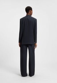 Navy pinstriped suit with a tailored blazer and wide-leg trousers, made from smooth fabric. The blazer features a notched collar and subtle stitching.