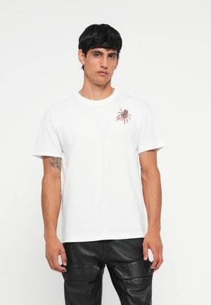 Weißes Baumwoll-T-Shirt mit einem grafischen Spinnenprint auf der linken Brust. Abgerundet mit kurzen Ärmeln und einem runden Ausschnitt.