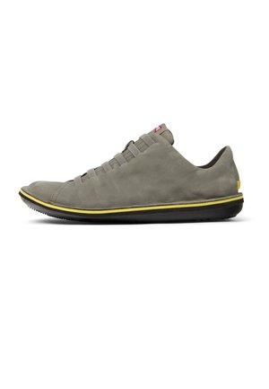 Zapatilla de ante gris con perfil bajo, punta redonda, cordones elásticos, detalle amarillo en la entresuela y suela exterior de goma negra texturizada.