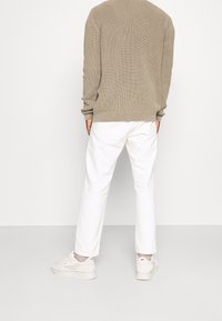 Pull en maille beige avec une texture côtelée, associé à un pantalon blanc. Les chaussures sont des baskets gris clair avec des accents subtils.