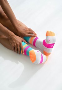 Bunte gestreifte Socken in Türkis, Weiß, Pink und Orange mit kontrastierenden einfarbigen Zehen. Sichtbare Etiketten an den Sohlen zeigen die Größen an.
