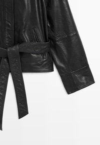 Giacca in pelle nera con vita con cintura, tasche laterali e una texture liscia con cuciture visibili. Progettata con una silhouette moderna.