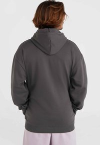 Šedá mikina vyrobená z měkké tkaniny, s velkou kapucí, žebrovanými manžetami a volným střihem. Zadní pohled ukazuje minimalistické designové detaily.