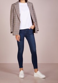 Károvaný blejzr v béžové a hnědé barvě, bílé tričko, tmavě modré skinny džíny a bílé tenisky, které ukazují uvolněný střih a klasický styl.