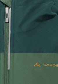 Grüne Reißverschlussjacke mit texturierter Oberfläche, ausgestattet mit einem zweifarbigen Design in dunkelgrün und hellgrün, sowie einem gestickten goldenen "Vaude"-Logo.