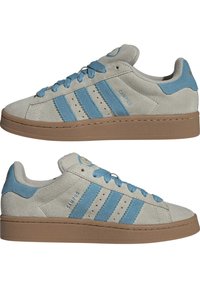 Graue Wildledersneaker mit blauen Akzenten, ausgestattet mit drei blauen Streifen, flachen Schnürsenkeln und einer braunen Gummisohle. Auffällige Perforationen im Obermaterial.