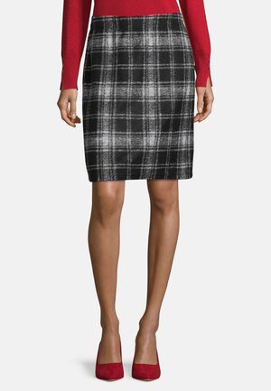 Kvinde iført sort- og hvidternet nederdel til knæet, rød bluse med lange ærmer og røde høje hæle, stående foran en hvid baggrund.