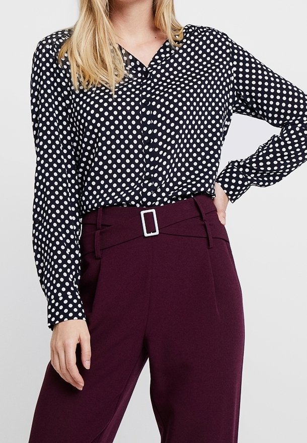 Blusa a righe bianche e nere con maniche lunghe e colletto, abbinata a pantaloni scuri bordeaux su misura con una fibbia rettangolare argentata.