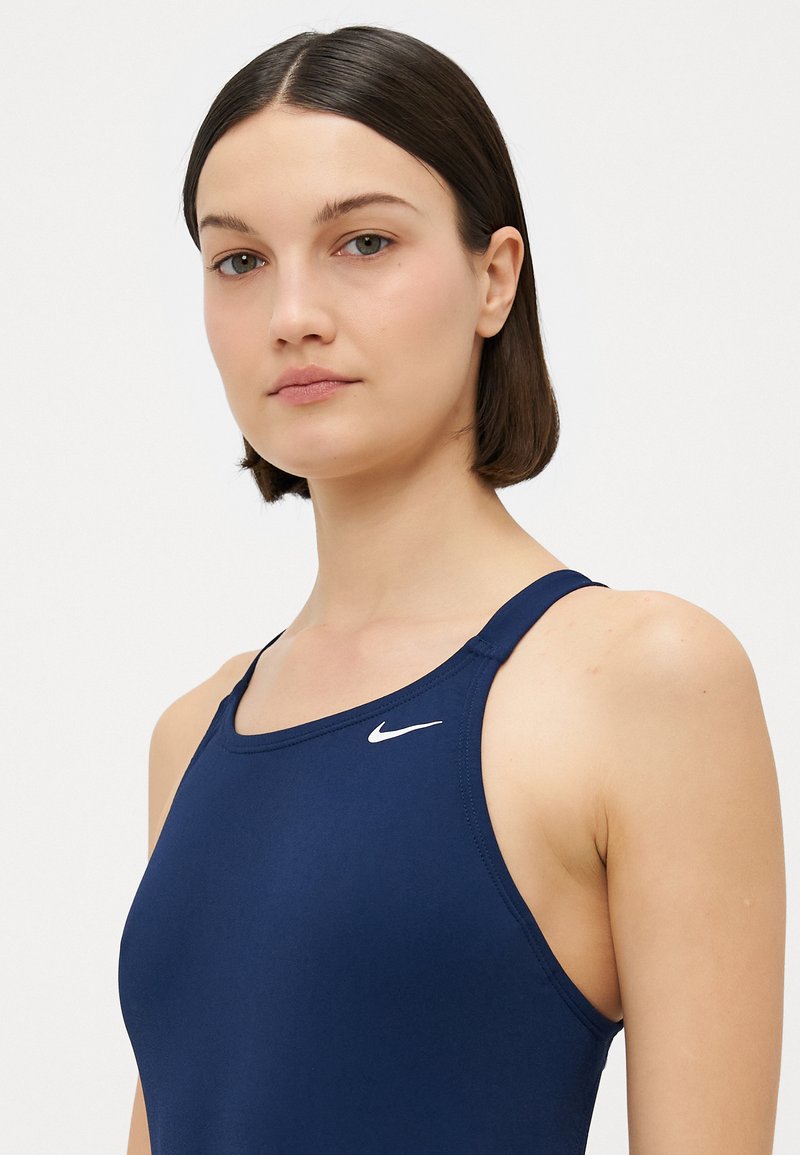 Marineblaues Sport-Top mit Rundhalsausschnitt und dünnen Trägern. Auf der Brust befindet sich ein kleines weißes Nike-Logo. Glatte Textur.