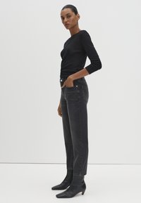 Woman standing wearing a black long-sleeve top, high-waisted faded black jeans, and black ankle boots with a small heel.