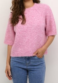 Maglione rosa lavorato a maglia con una vestibilità comoda, maniche corte e orlo a coste. Indossato sopra jeans blu, che mostrano una consistenza soffice.