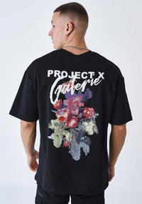Zwarte katoenen T-shirt met een grote bloemenafbeelding in kleuren zoals rood, paars en groen, met de tekst "PROJECT X" en "Galerie" in het wit.