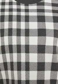 Pull en noir et blanc à motifs avec un design en damier composé de carrés unis et rayés alternés. Texture en maille douce.
