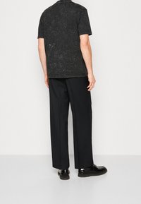 Svart texturerad kortärmad skjorta med avslappnad passform, tillsammans med lösa svarta byxor och glänsande svarta skor.