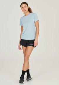Lyseblå atletisk t-shirt lavet af glat stof, parret med sorte shorts. Har en rund halsudskæring og korte ærmer, minimal branding.