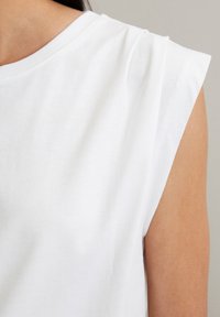 Witte top met korte mouwen, voorzien van een ronde halslijn en gestructureerde schouderdetails. Gemaakt van glad katoen met een relaxte pasvorm.