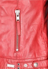 Punainen nahkatakki, jossa on hopeinen vetoketju, näkyvät saumat ja metalliset yksityiskohdat. Pintakäsittely on sileä, hieman kulunut ulkonäöltään.