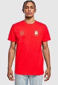 Raudonas medvilninis marškinėliai su auksiniu Portugalijos emblemą ir herbu kairėje krūtinės pusėje. Trumpomis rankovėmis, apvaliu kaklu, laisvo kirpimo.