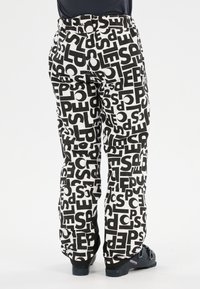 Zwart-witte sneeuwbroek met een geometrisch patroon en gedurfde tekstgraphics, met een losse pasvorm, riemlussen en stevige zwarte schoeisel.