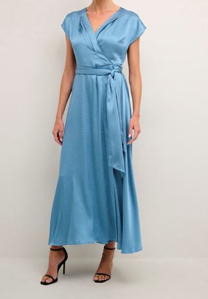 Femme portant une robe portefeuille en satin bleu clair à manches courtes avec une ceinture nouée à la taille, associée à des sandales noires à talons hauts.