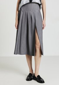 Gonna midi grigia a righe con spacco frontale indossata con mocassini neri e un top senza maniche.