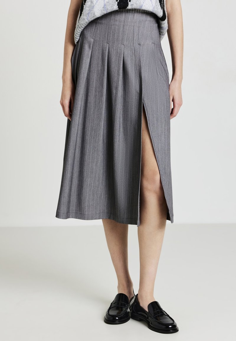 Gonna midi grigia a righe con spacco frontale indossata con mocassini neri e un top senza maniche.