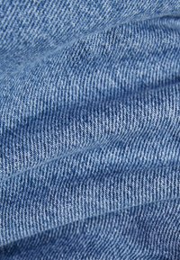 Tissu en denim de couleur bleu clair avec un tissage en sergé fin, présentant une légère texture et des plis, mettant en valeur sa nature douce et flexible.