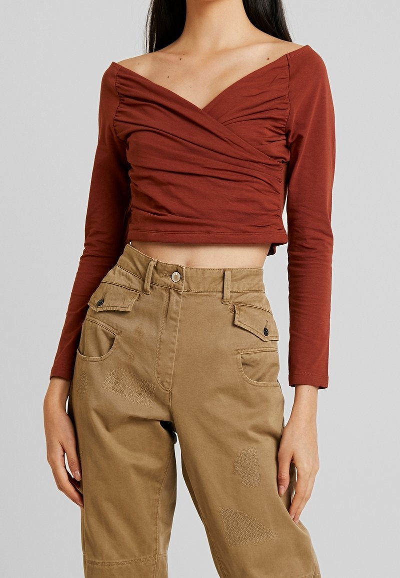 Rostroter, langärmeliger Croptop mit Wickeldesign und gerafftem Stoff am Dekolleté, kombiniert mit khakifarbenen Hosen mit Patchdetails und Taschen.