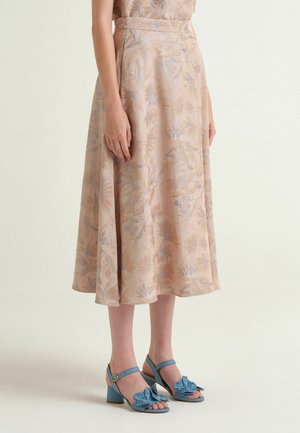 Gonna beige a fiori di lunghezza media indossata da persona in piedi, abbinata a sandali blu con tacco e dettagli a fiocco.