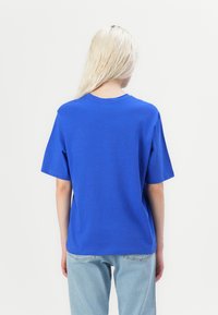 Blauwe katoenen t-shirt met korte mouwen, ontspannen pasvorm, ronde halslijn en een gladde textuur. Draagt met lichtblauwe jeans, met een eenvoudig ontwerp aan de achterkant.