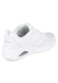 Chaussure de sport blanche avec une tige en cuir lisse et en mesh, détails perforés, col rembourré et semelle extérieure épaisse translucide avec un système de coussin d'air.