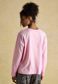 Pink long-sleeve cotton t-shirt with a crew neck and relaxed fit. Features stitched detailing. Paired with floral patterned pants.