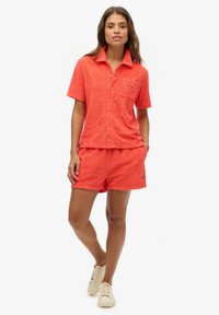 Chemise à manches courtes texturée orange et short assorti, avec un design à boutons et une petite poche poitrine avec broderie de logo.