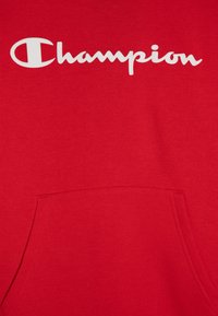 Felpa rossa realizzata in morbido cotone. Presenta un logo bianco "Champion" sul petto, una tasca a marsupio e polsini a coste.