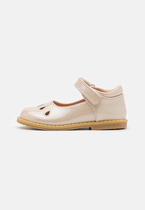 Chaussure Mary Jane en cuir verni beige avec des découpes, une sangle réglable et une semelle en caoutchouc. Présente un bout arrondi et des accents cousus.