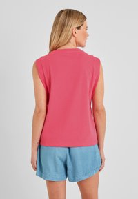 Sleeveless pink cotton top with a rounded neckline and relaxed fit, paired with denim shorts. Smooth texture, simple design, no visible patterns.