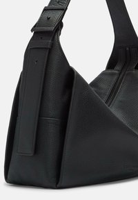 Sac en cuir noir à bandoulière présentant une finition texturée, un design anguleux, une sangle ajustable et une poche zippée.