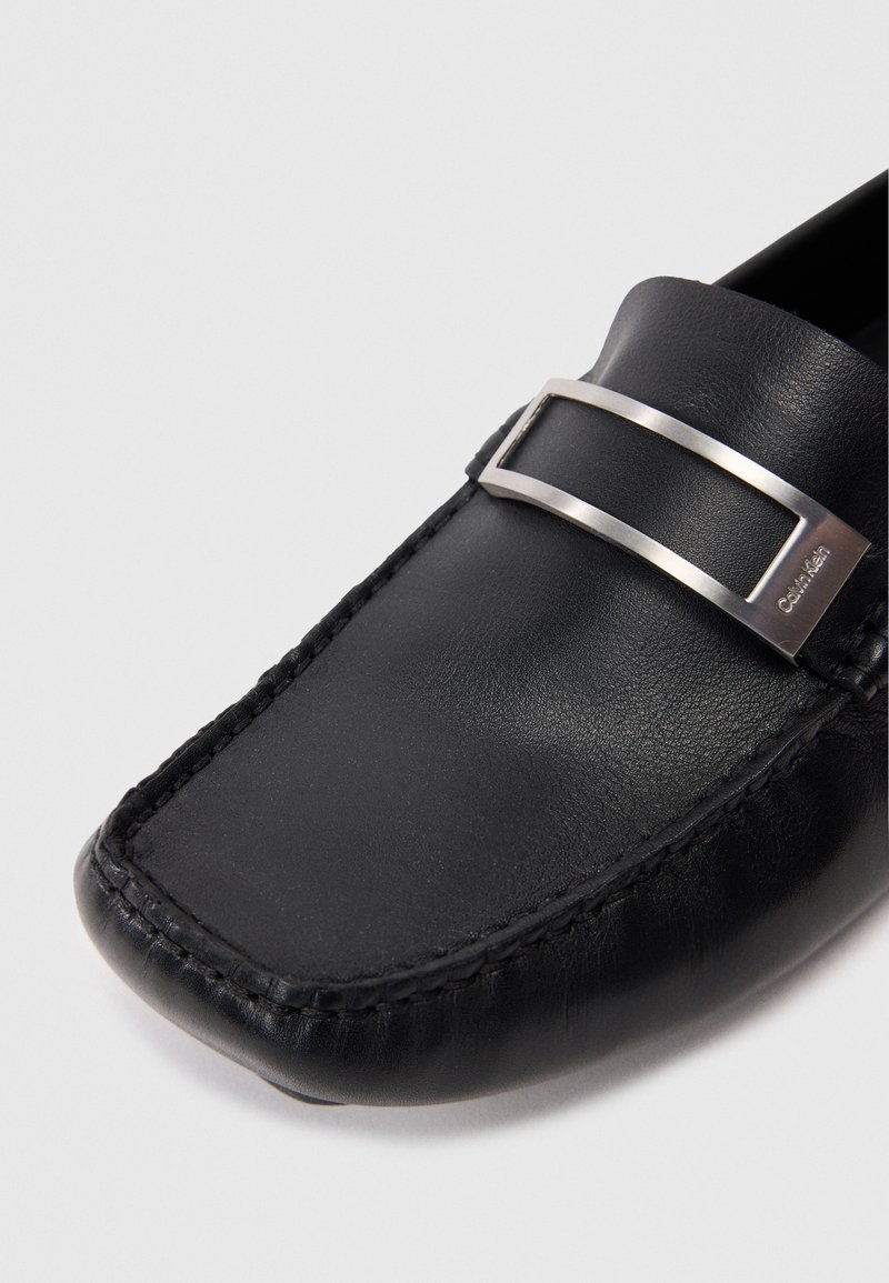 Schwarze Lederlommer mit flacher Form, ausgestattet mit einem silbernen metallic Akzent und detaillierten Nähten entlang der Kanten.