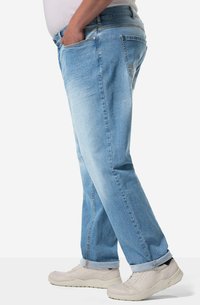 Jeans de mezclilla azul claro con un corte relajado, que presentan dos bolsillos frontales y un dobladillo enrollado. Combinados con zapatillas deportivas de colores claros.