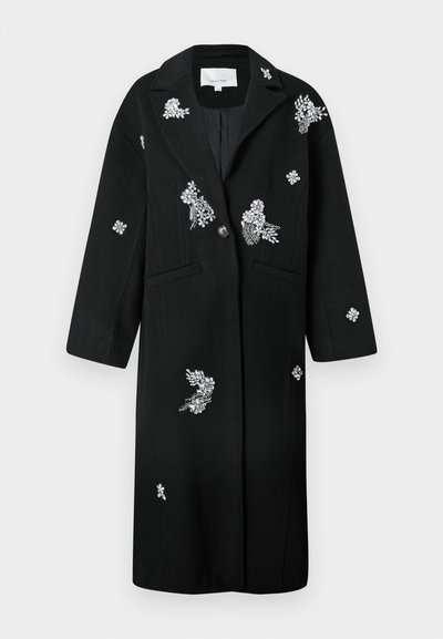 Črn plašč z izbrano srebrno cvetlično vezenino, strukturiranimi reverji, enostranskim zapiranjem na gumb in dvema sprednjima žepoma. Gladka tkanina s prilagojeno obliko.
